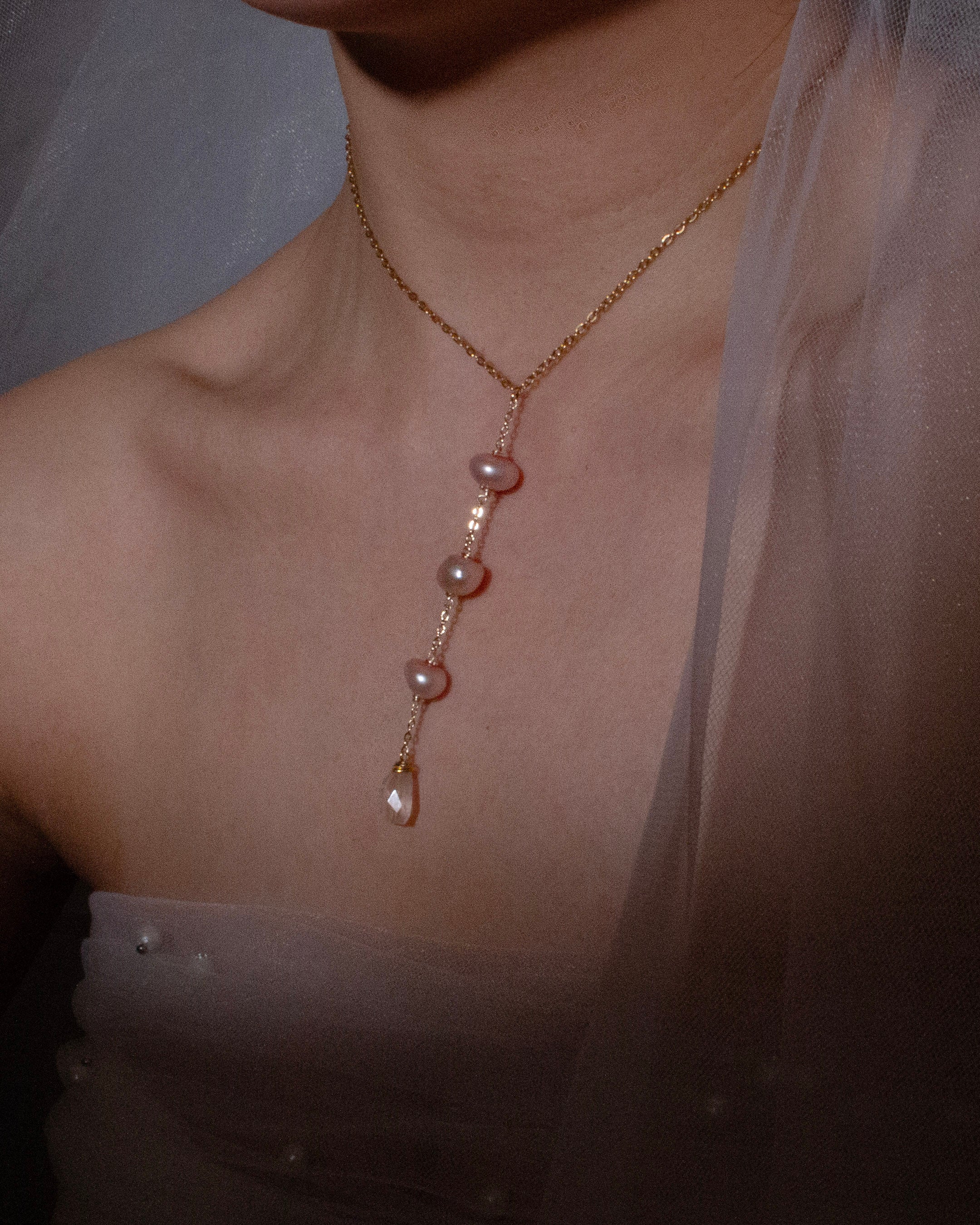 Gold necklace with pearls on a person wearing a sheer top.