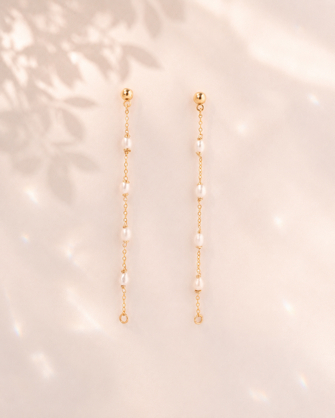 Gold earrings with pearl beads on a soft pink background