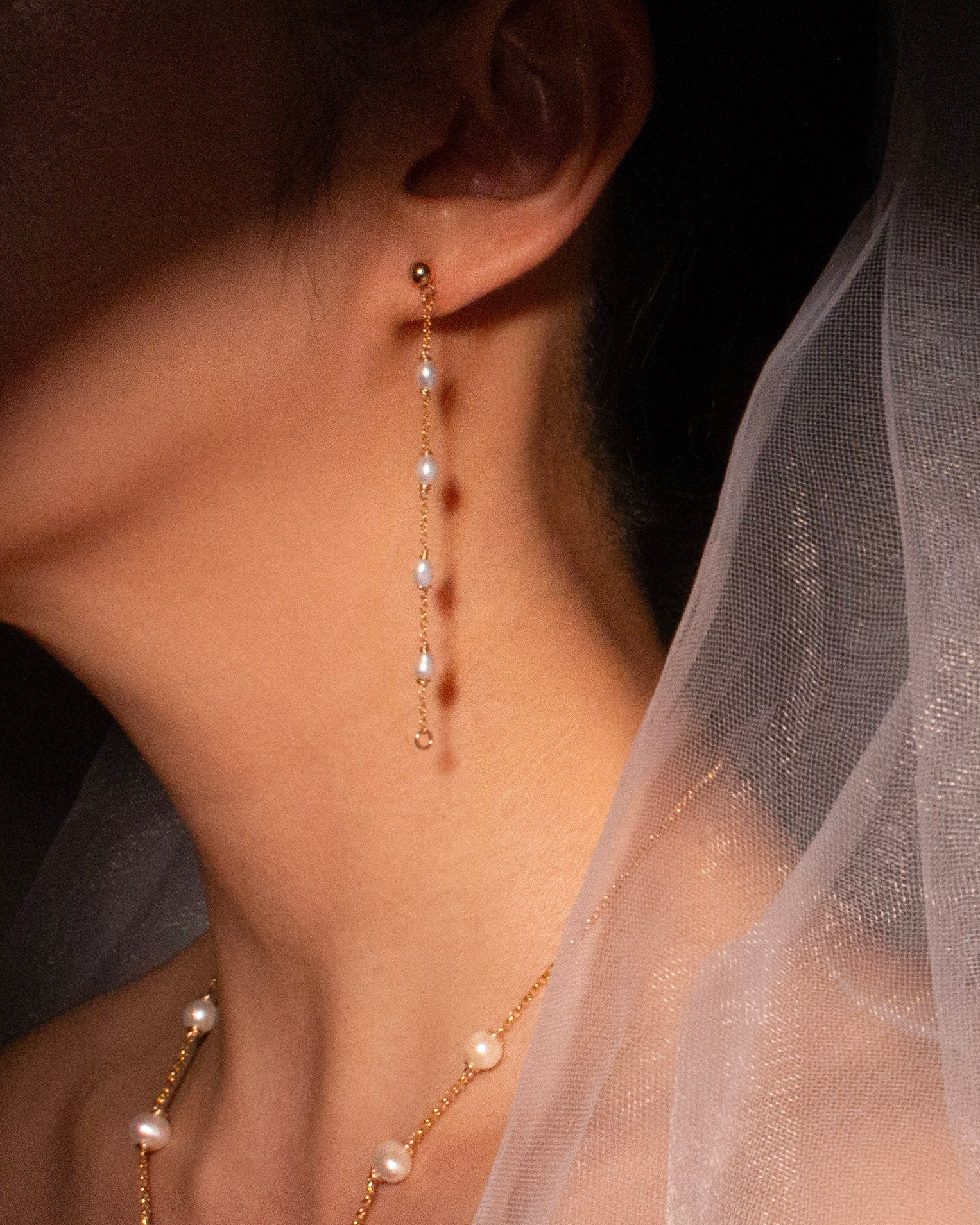 Pearl necklace and earrings worn by a person with a veil, highlighting jewelry details.