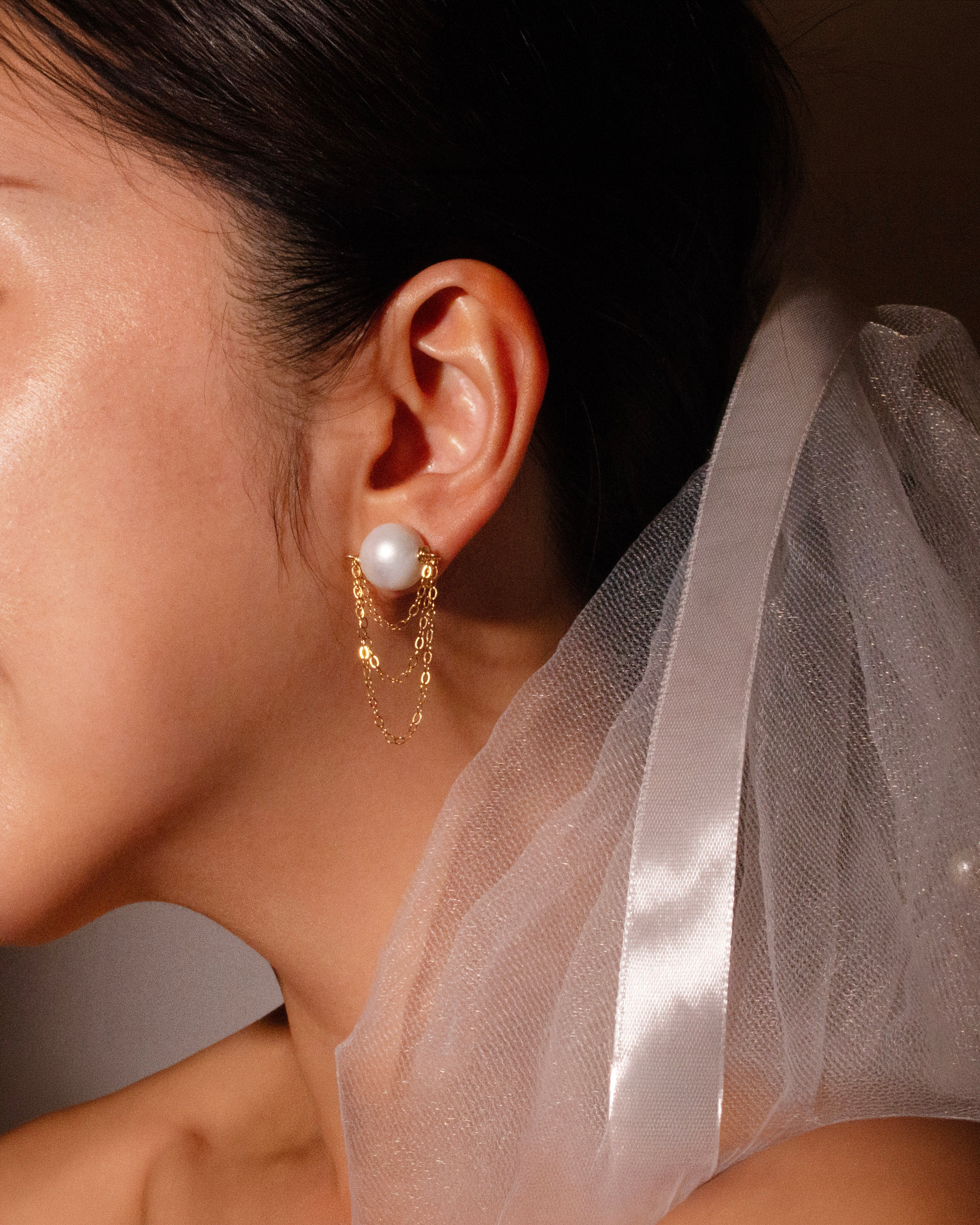 Close-up of a woman wearing pearl earrings with a veil in the background