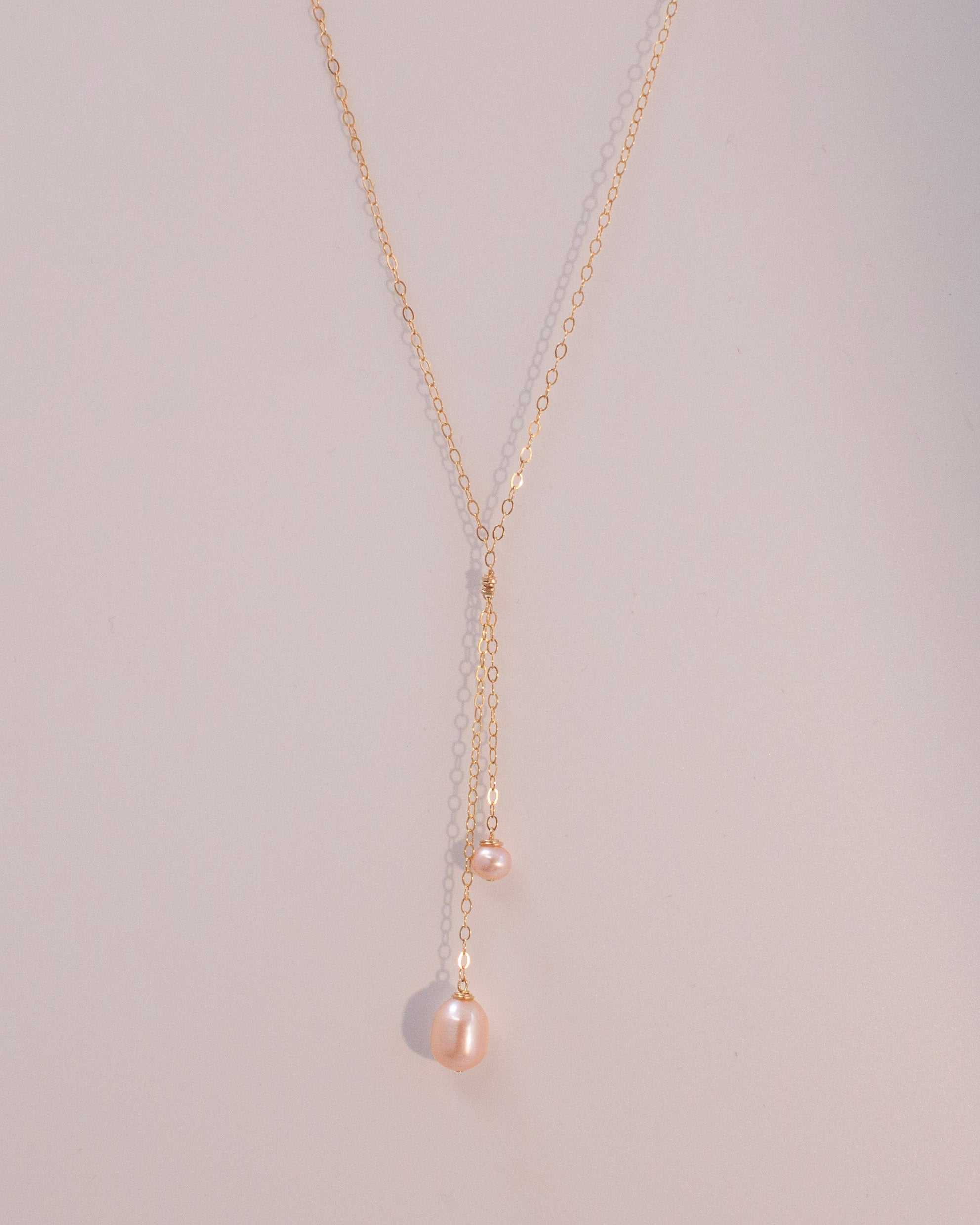 Delicate gold necklace with pink pearls pendant on a light gray background