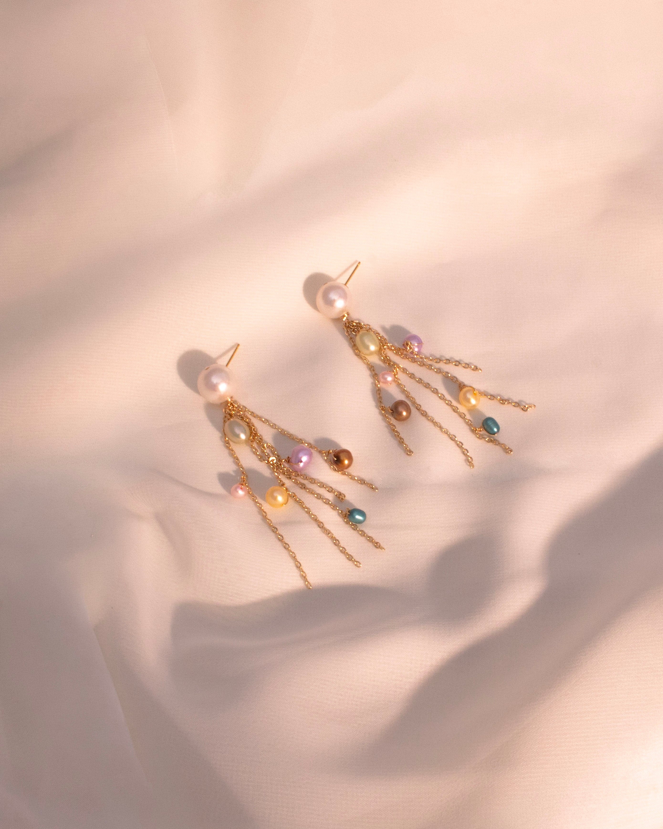 Gold earrings with colorful beads on a soft pink background