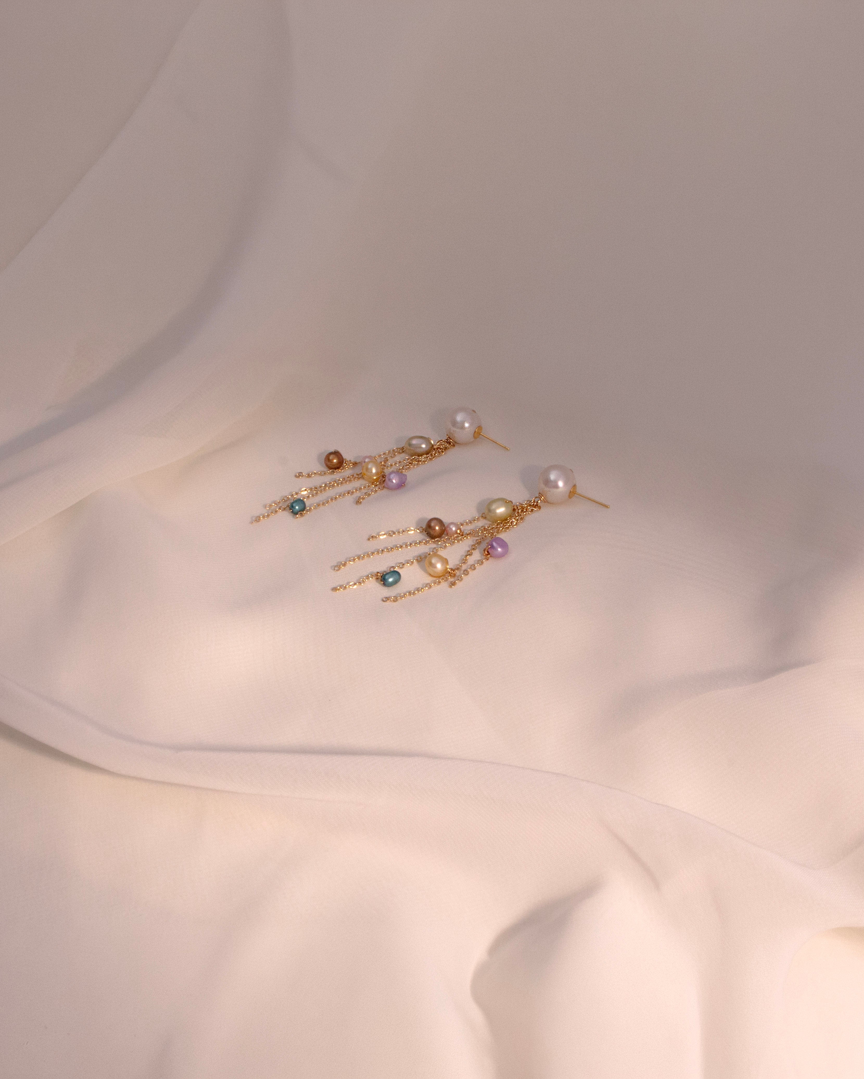 Pair of gold earrings with pearls and gemstones on a white fabric background