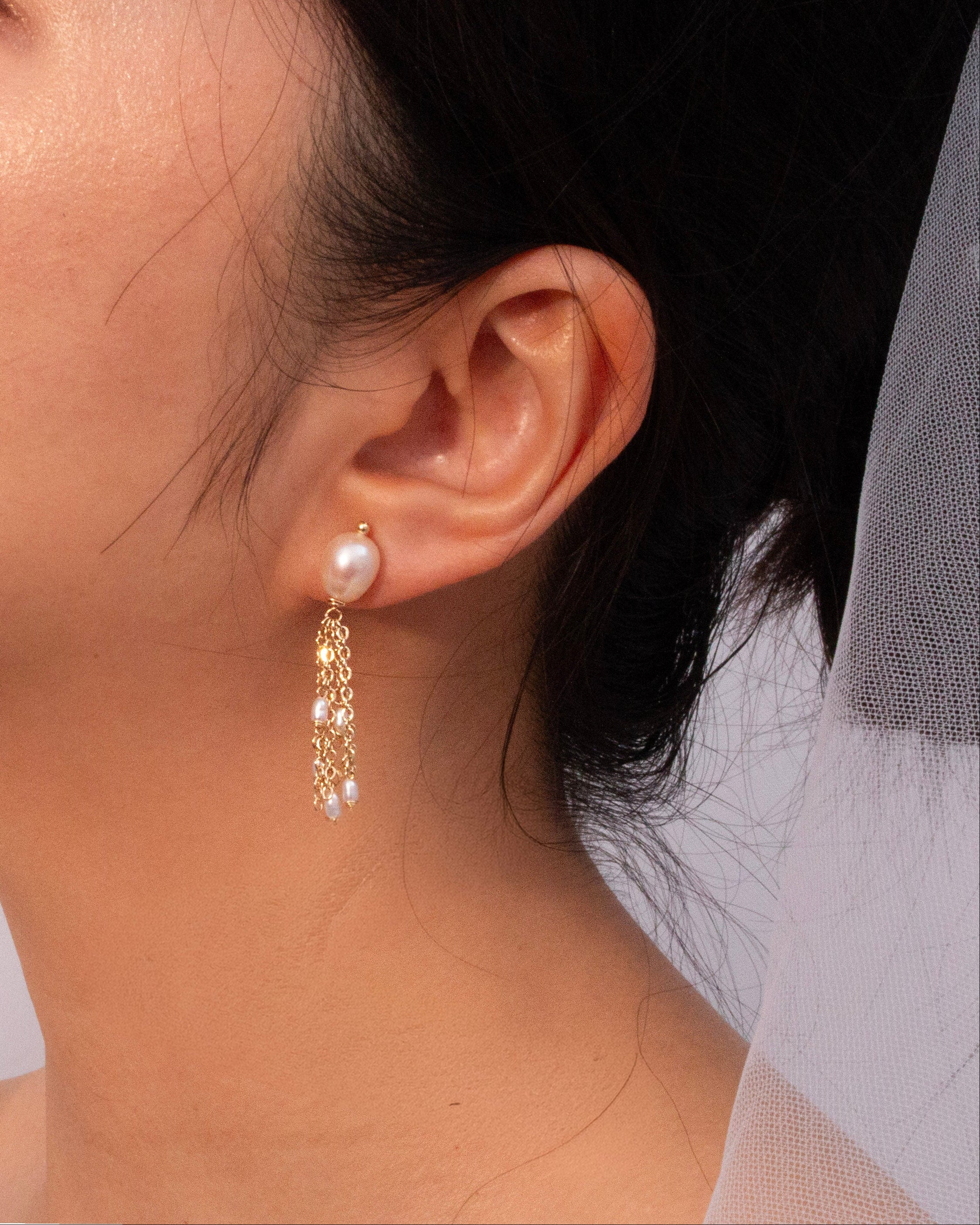 Close-up of an ear wearing a gold earring with pearls.