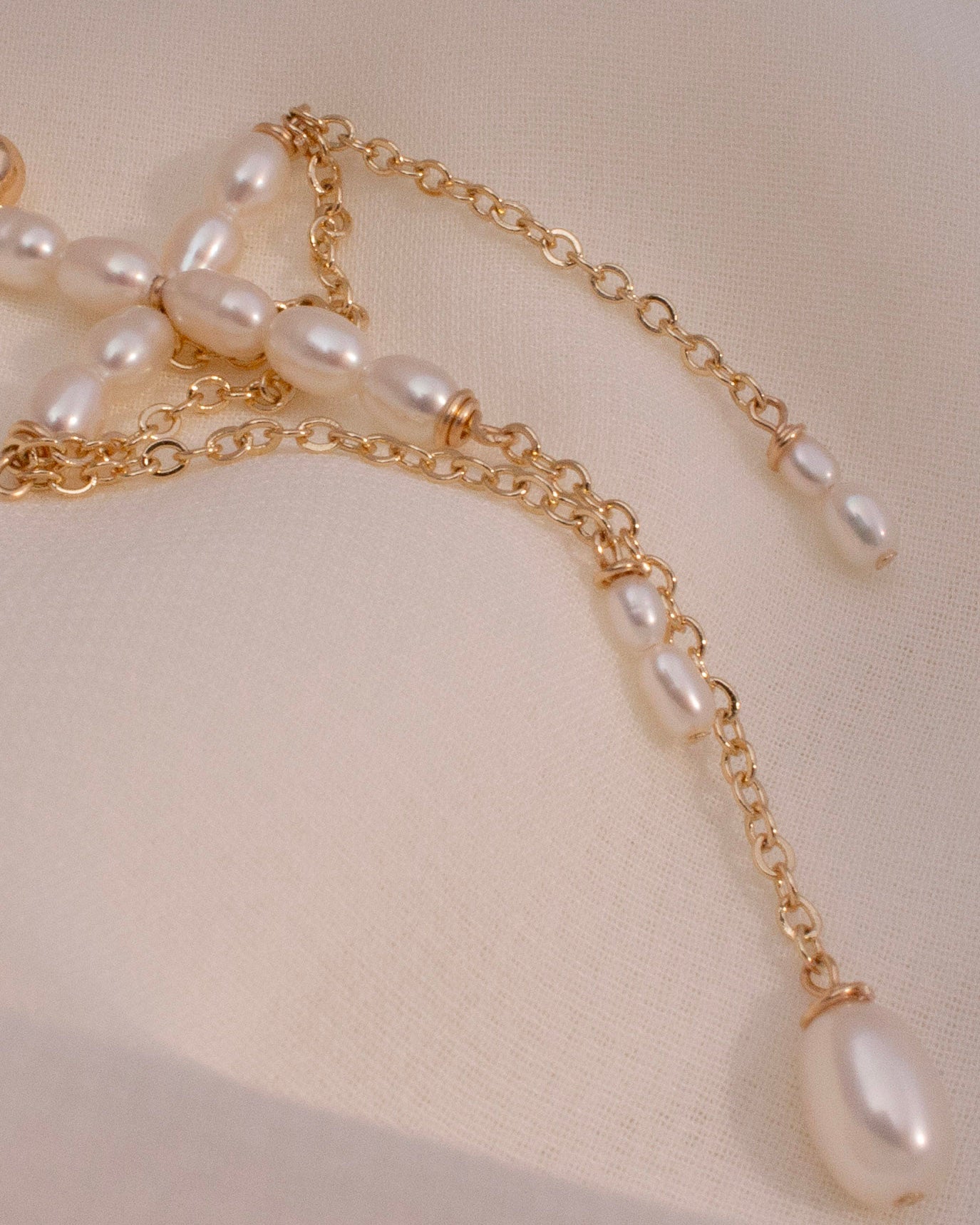 Gold chain earring with pearls on a beige fabric background