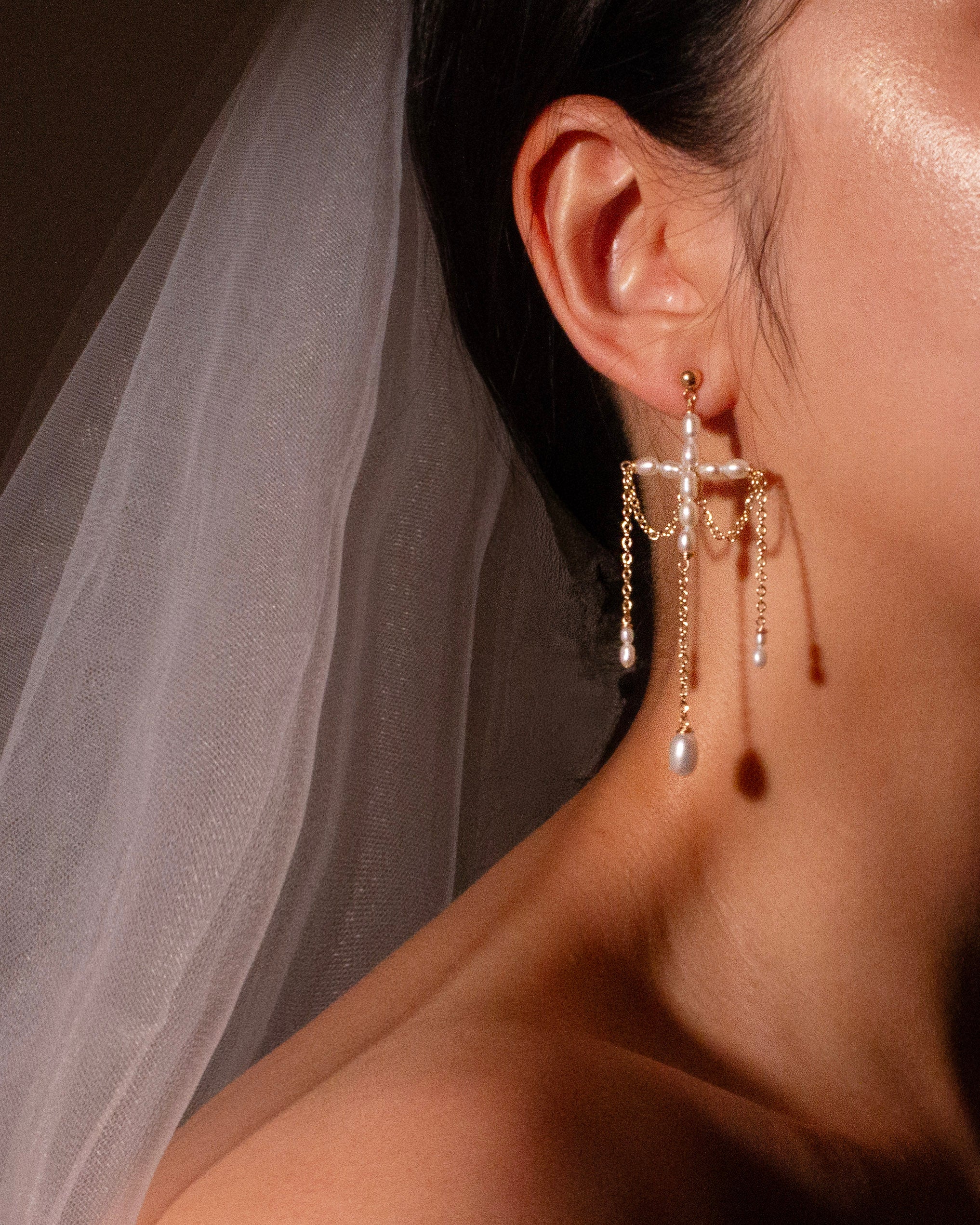 Close-up of a person wearing a delicate earring with a veil in the background