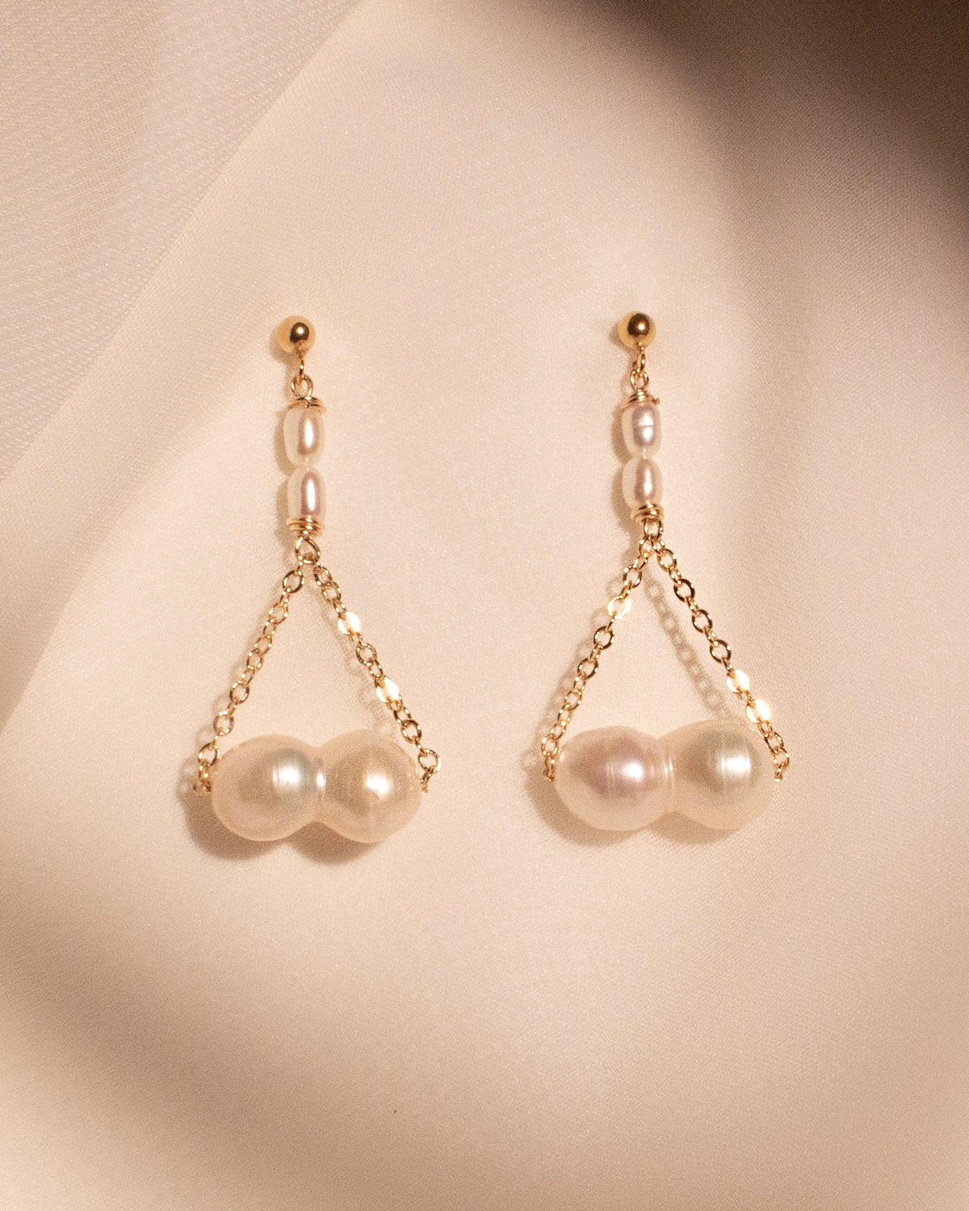 Pearl earrings with gold chains on a beige background