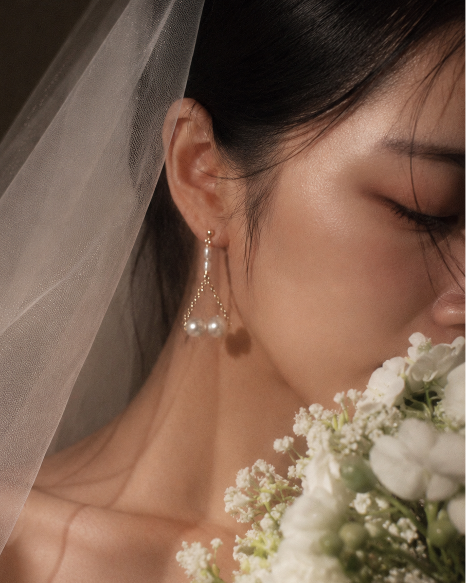 Close-up of a woman wearing pearl earrings with a veil and flowers in the background
