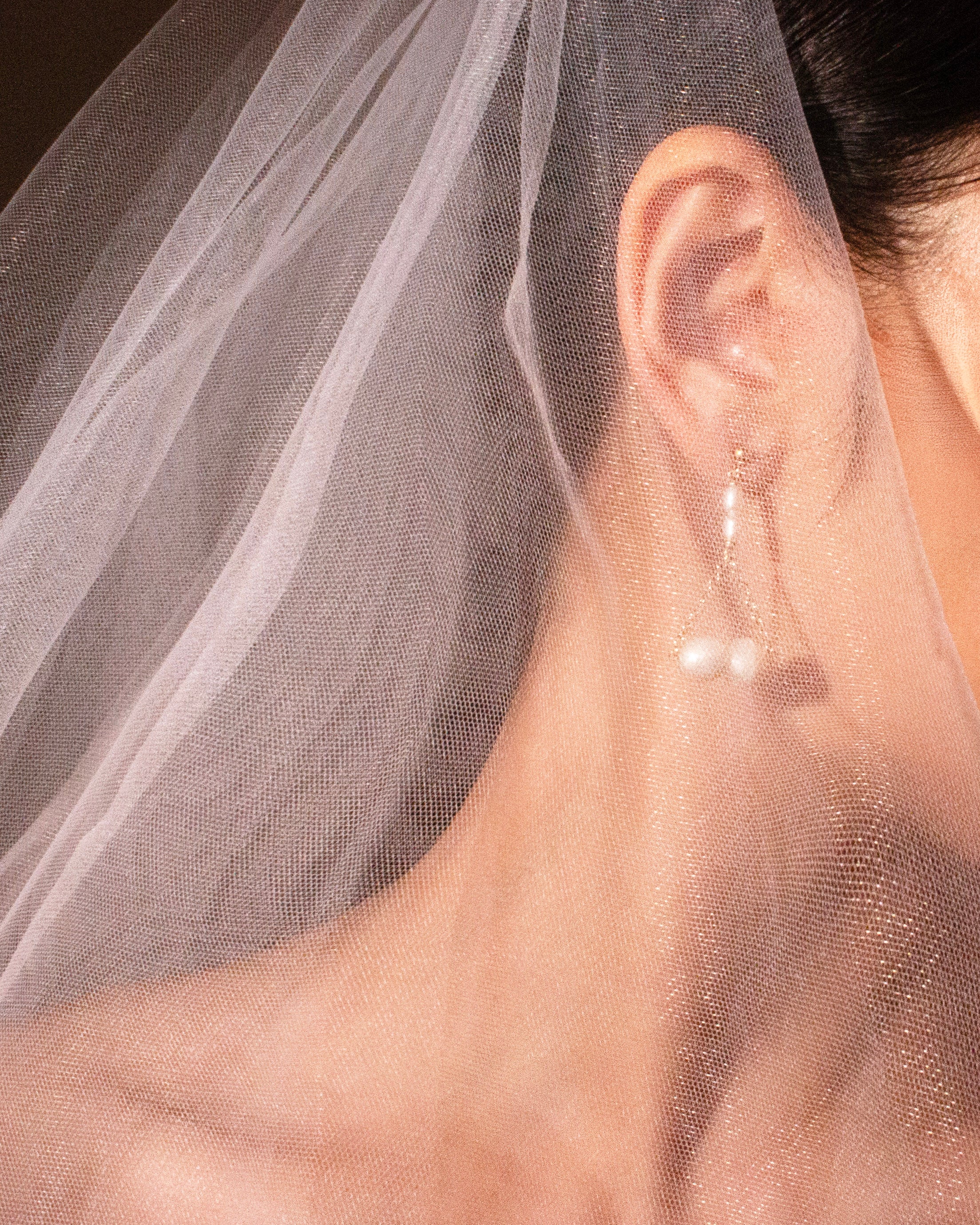 Close-up of a person wearing pearl earrings and a veil with a focus on an earring.