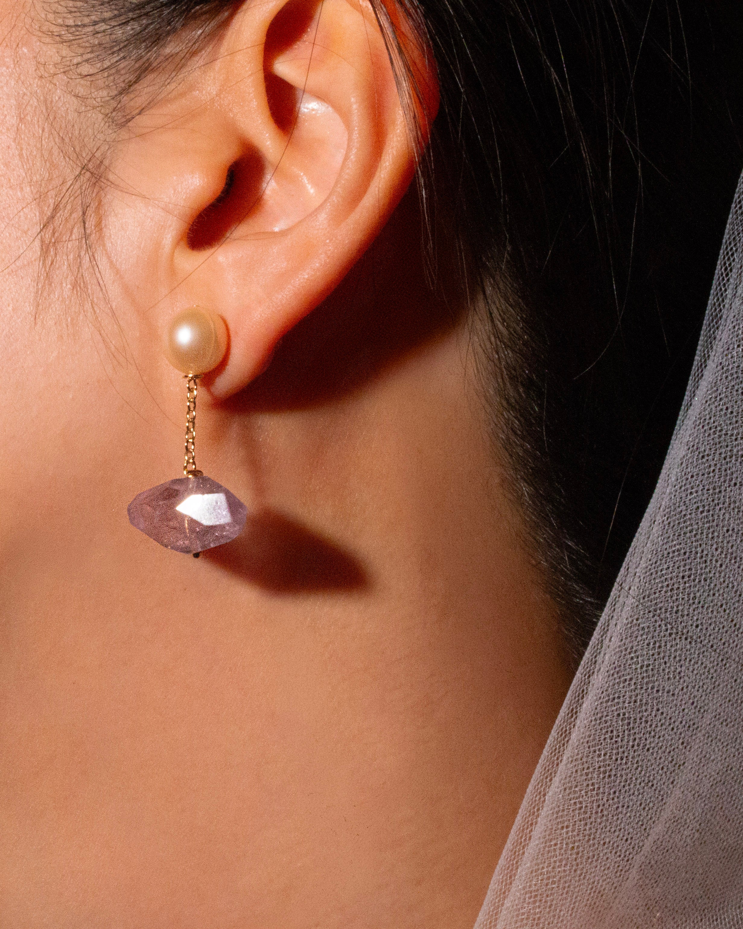 Close-up of wearing a dangling pearl earring with a amethyst gemstone.
