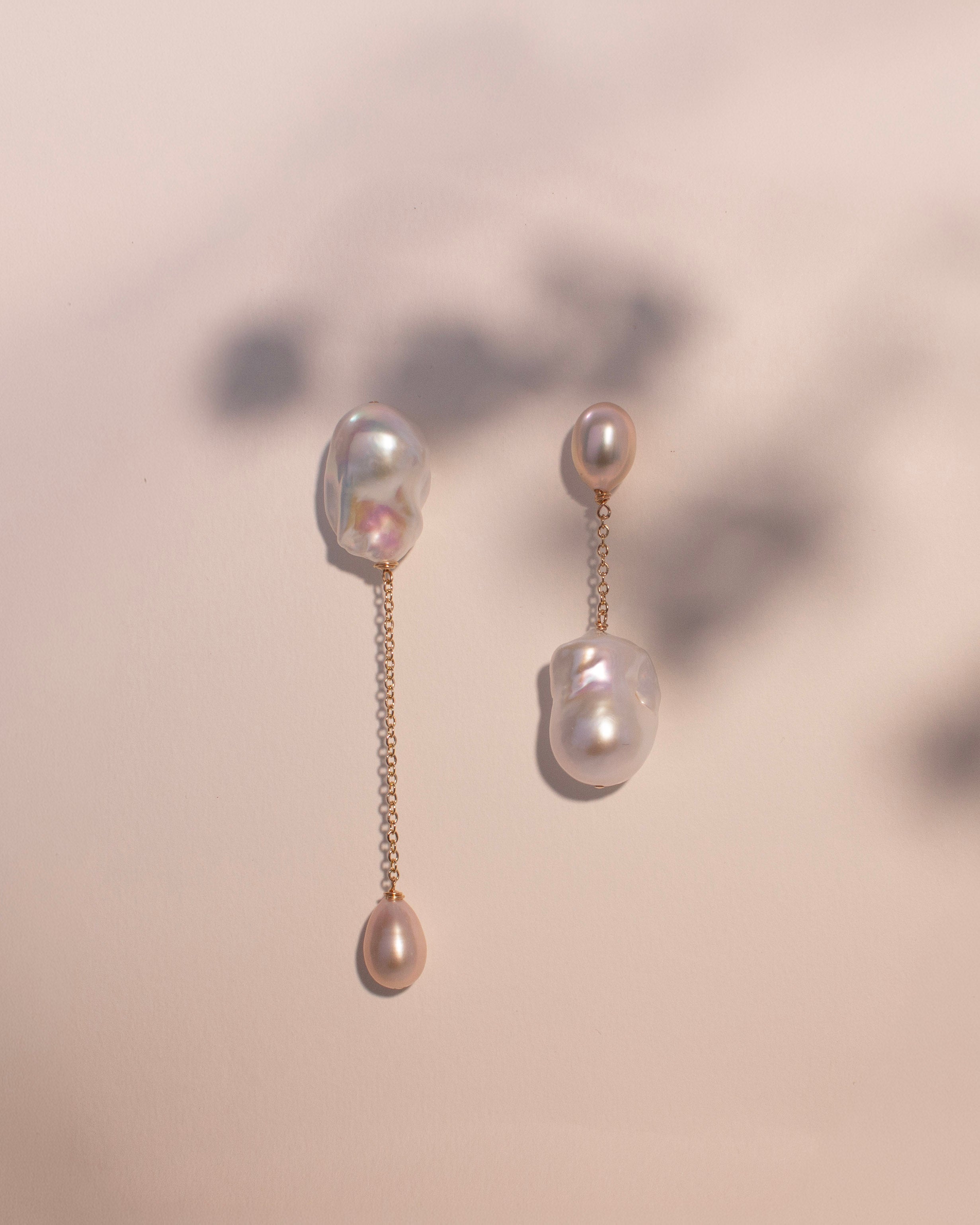 Pair of baroque pearl earrings with gold chains on a beige background