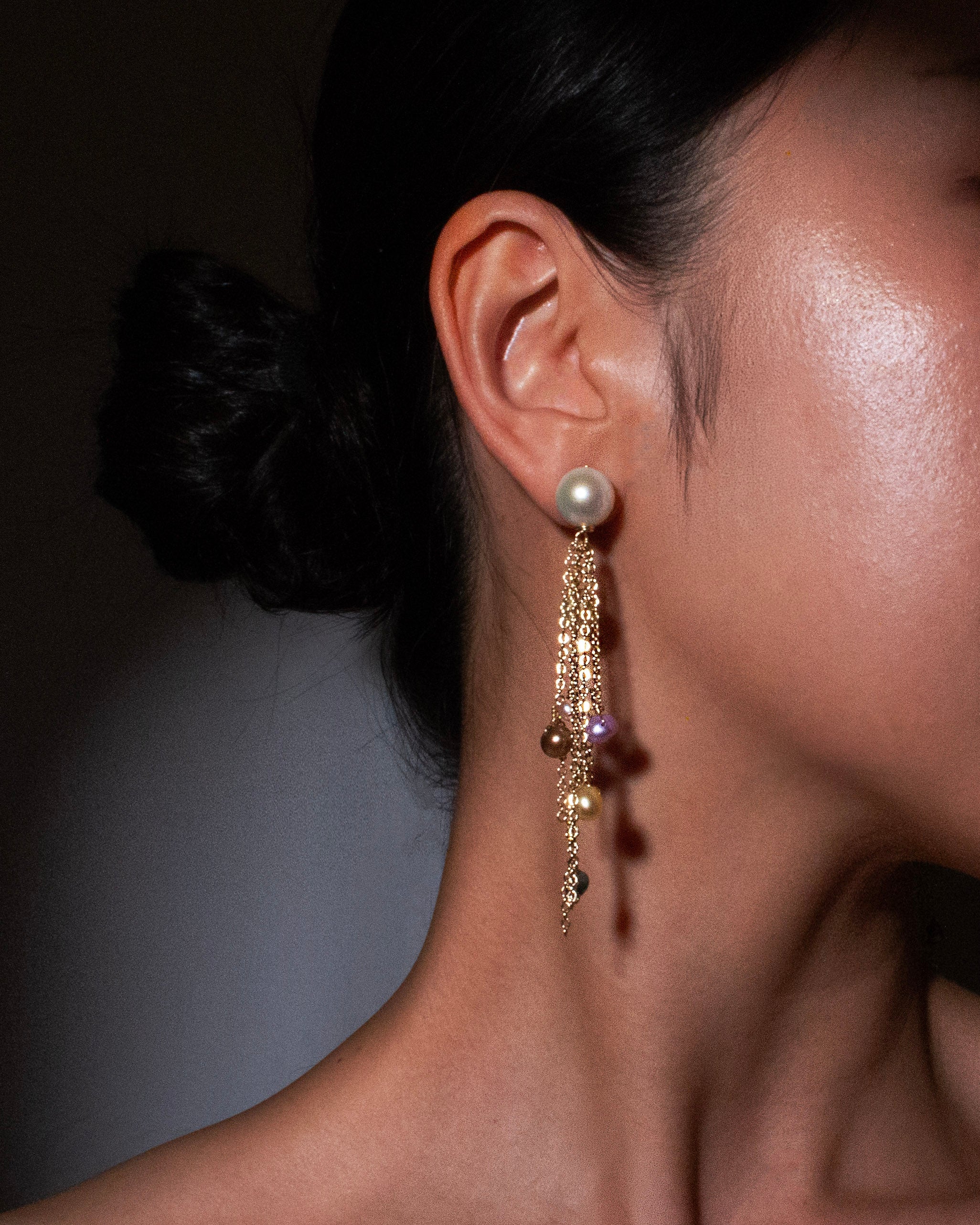 Close-up of a person wearing a pearl earring with gold accents against a neutral background