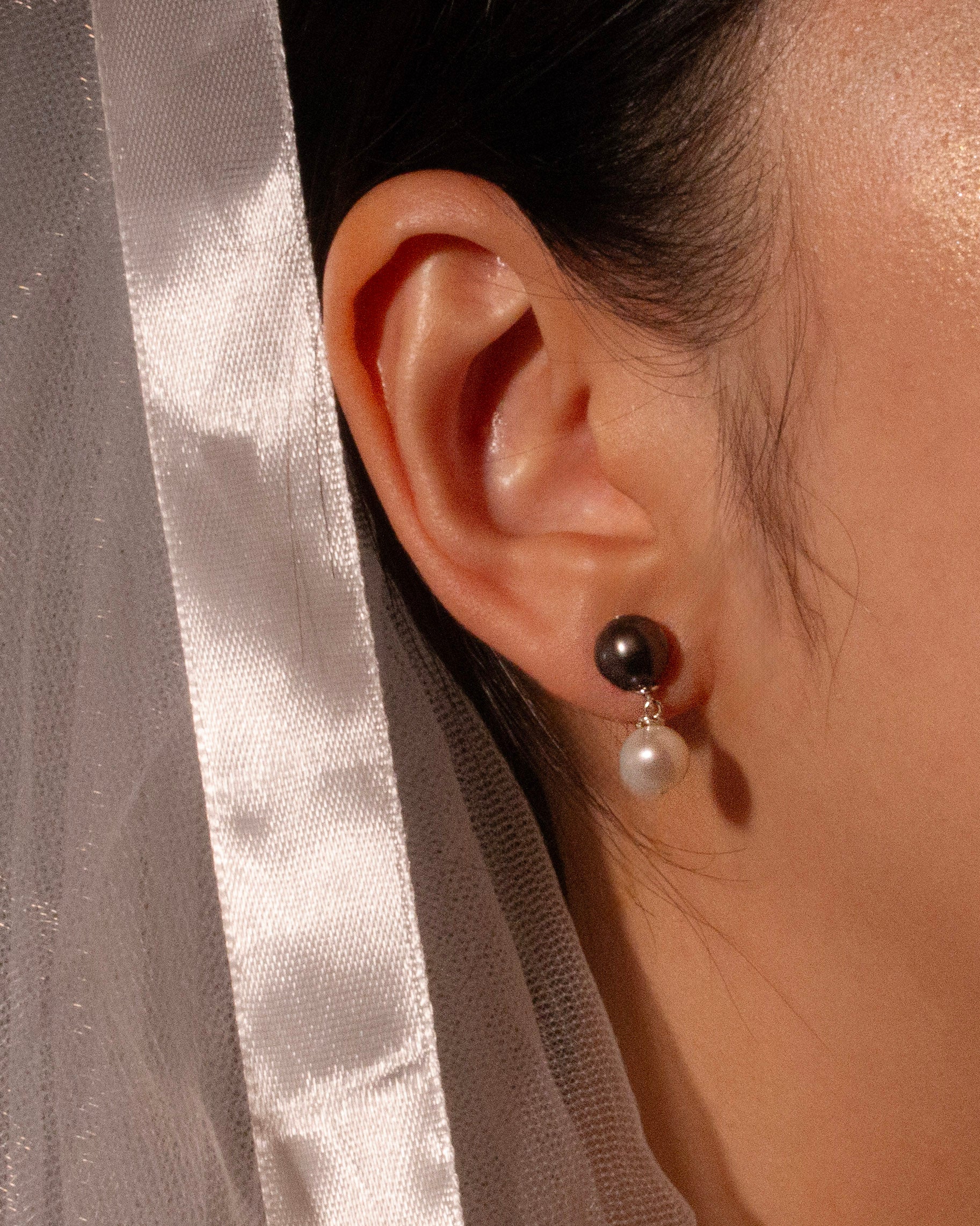 Close-up of an ear wearing a black and white pearl earring with a neutral background.