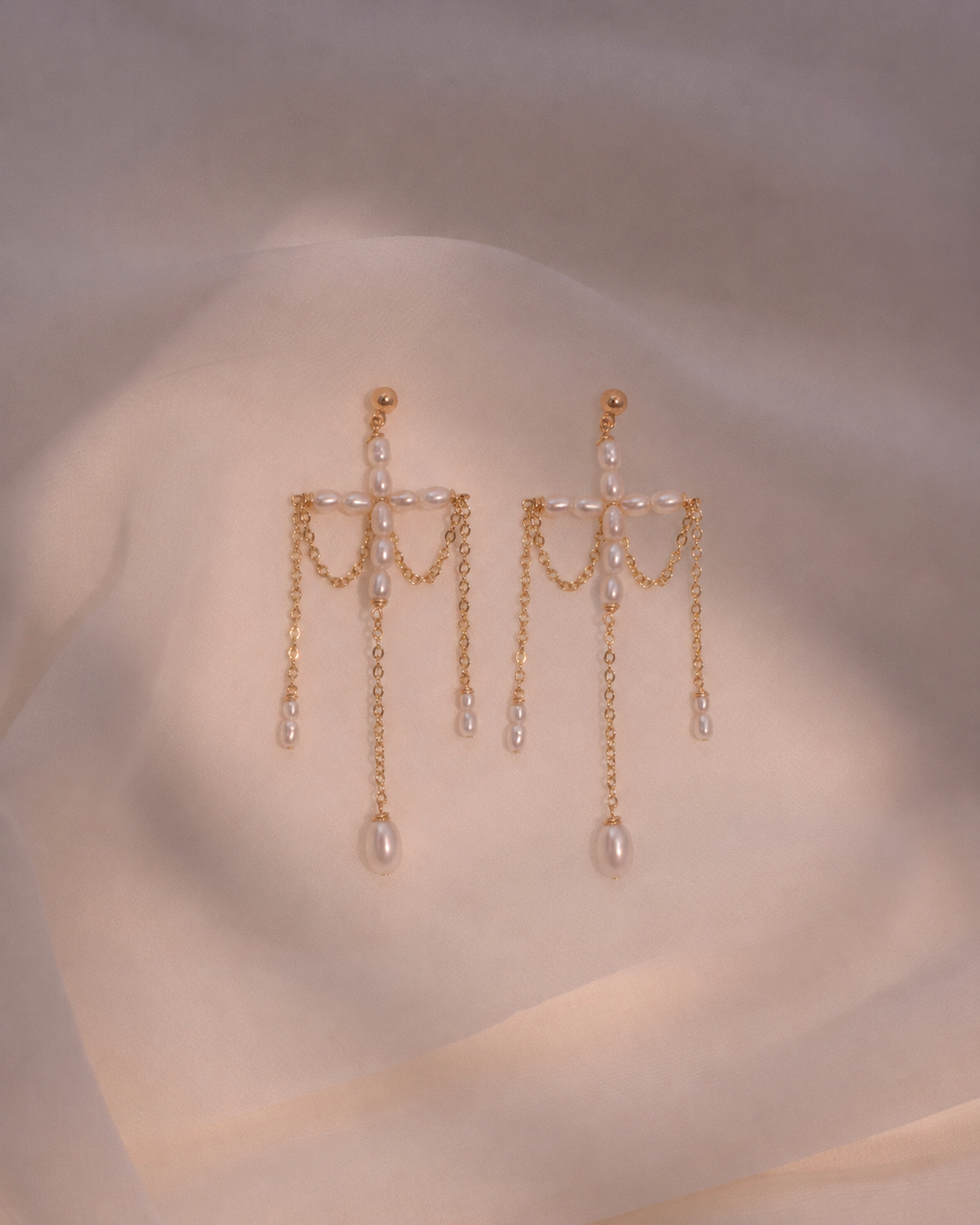 Gold earrings with chain and pearl details on a soft beige background