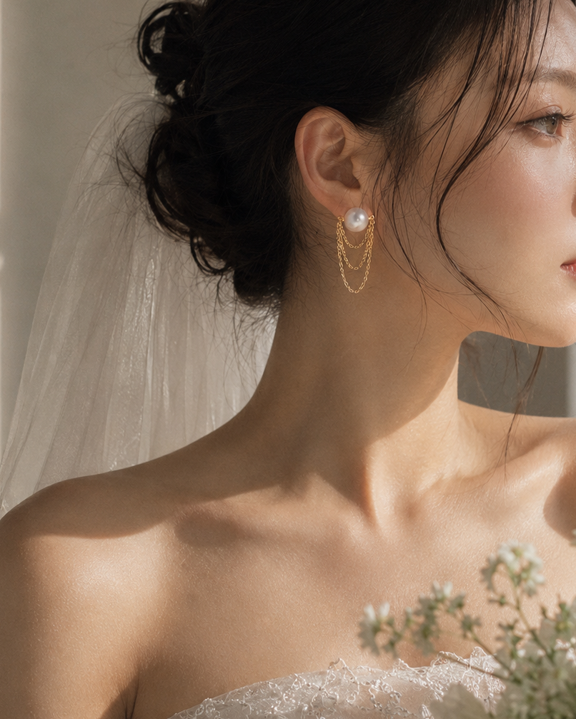 Close-up of a bride wearing gold hoop earrings with pearls, with a blurred background.