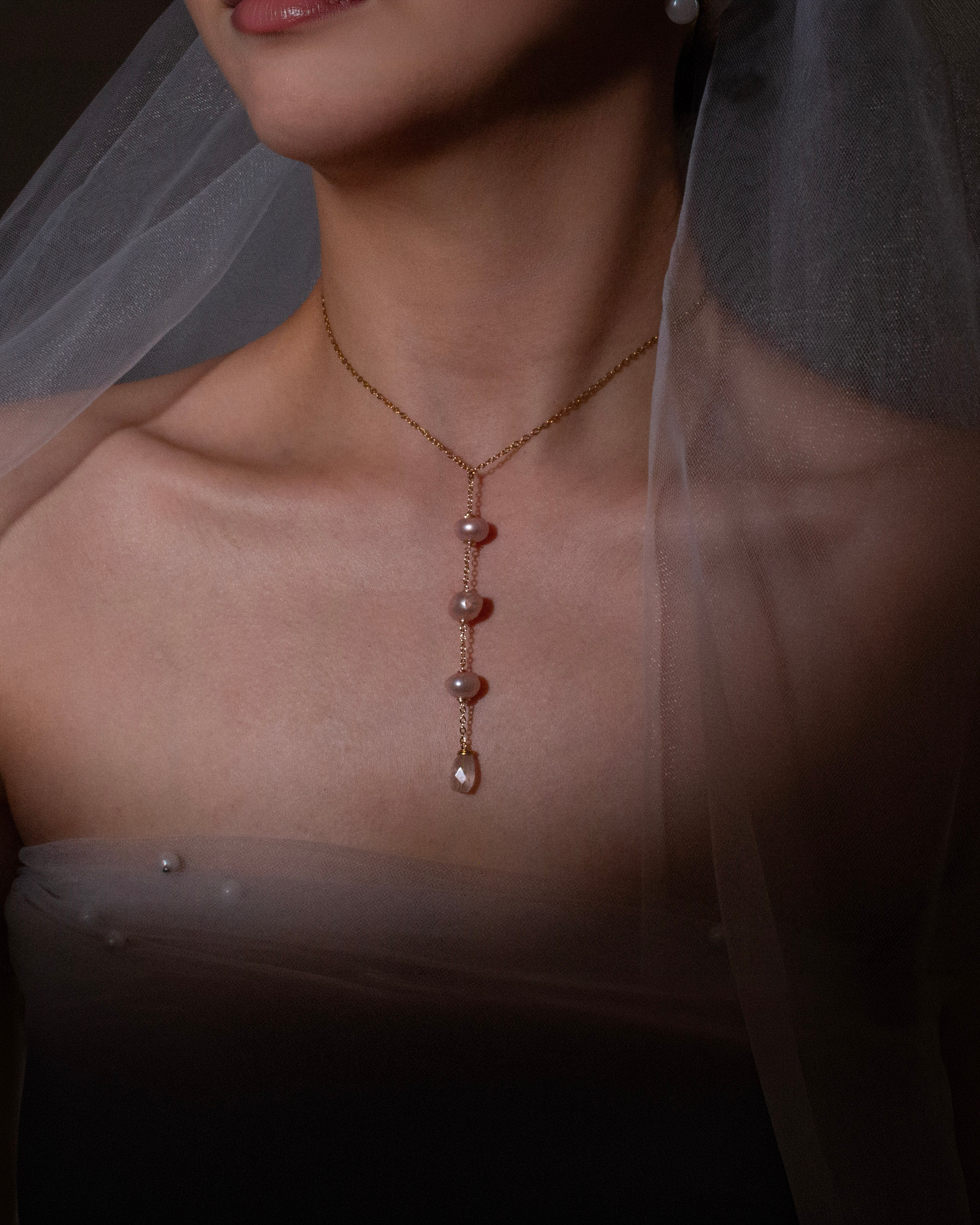 Close-up of a necklace with a pendant worn by a person with a veil, on a dark background