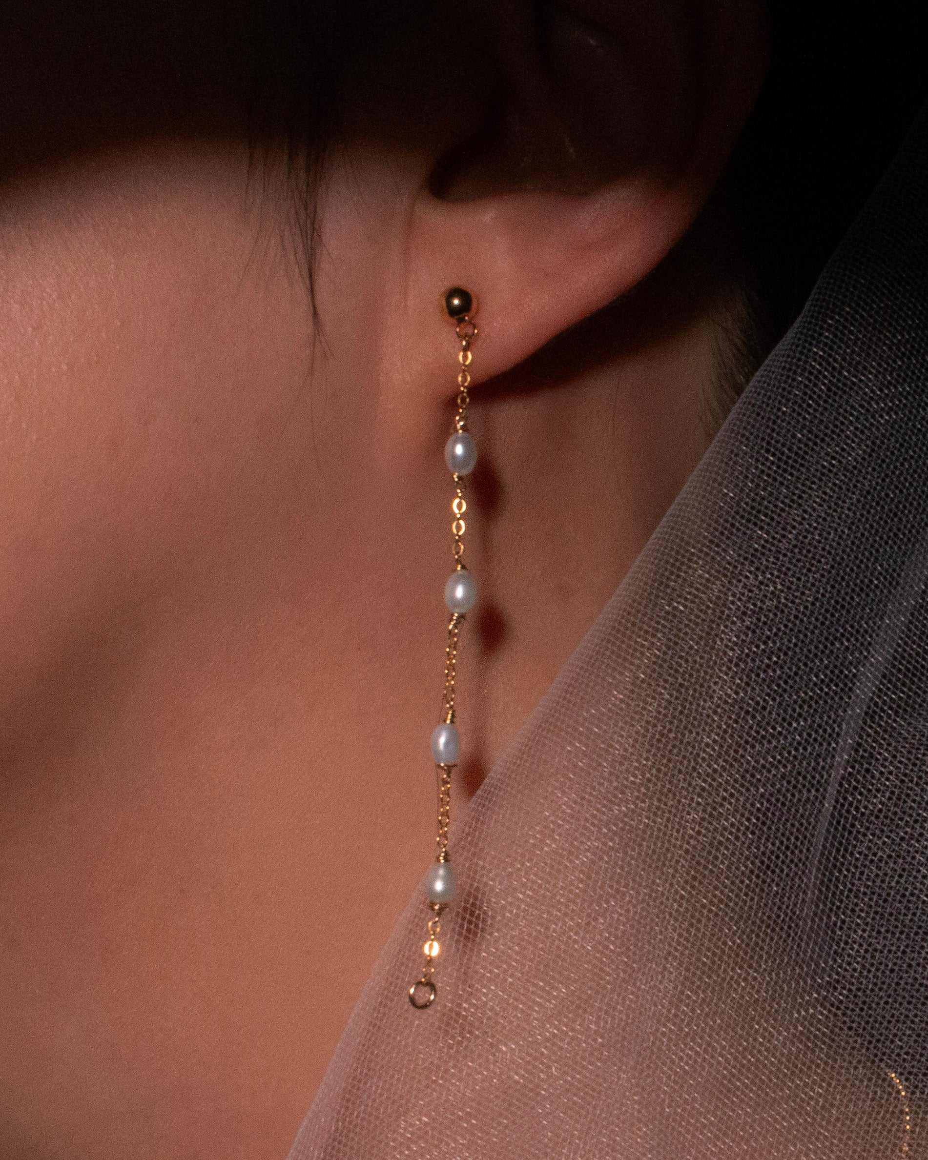 Pearl and gold earring worn by a person with a dark background