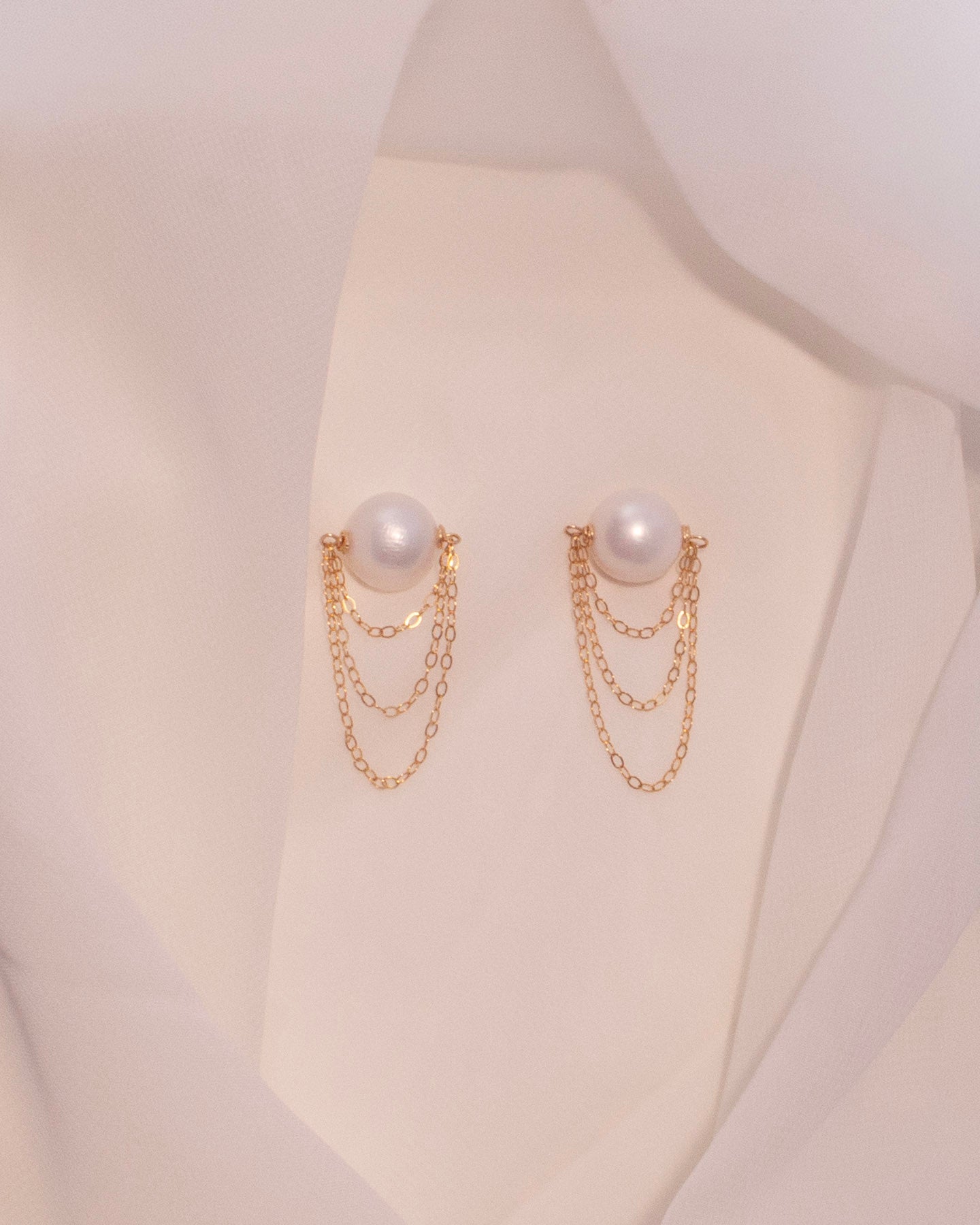 Pair of pearl earrings with gold chains on a mannequin bust.