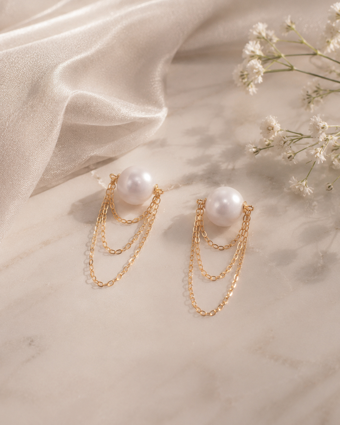 Pearl earrings with gold chains on a soft fabric background