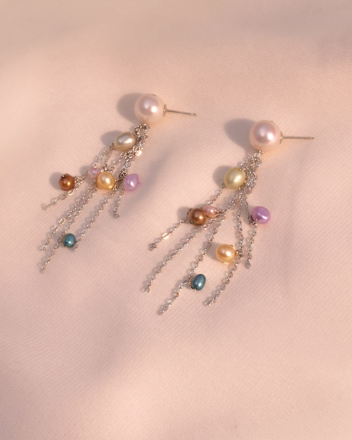 Pair of earrings with multicolored beads on a soft pink background