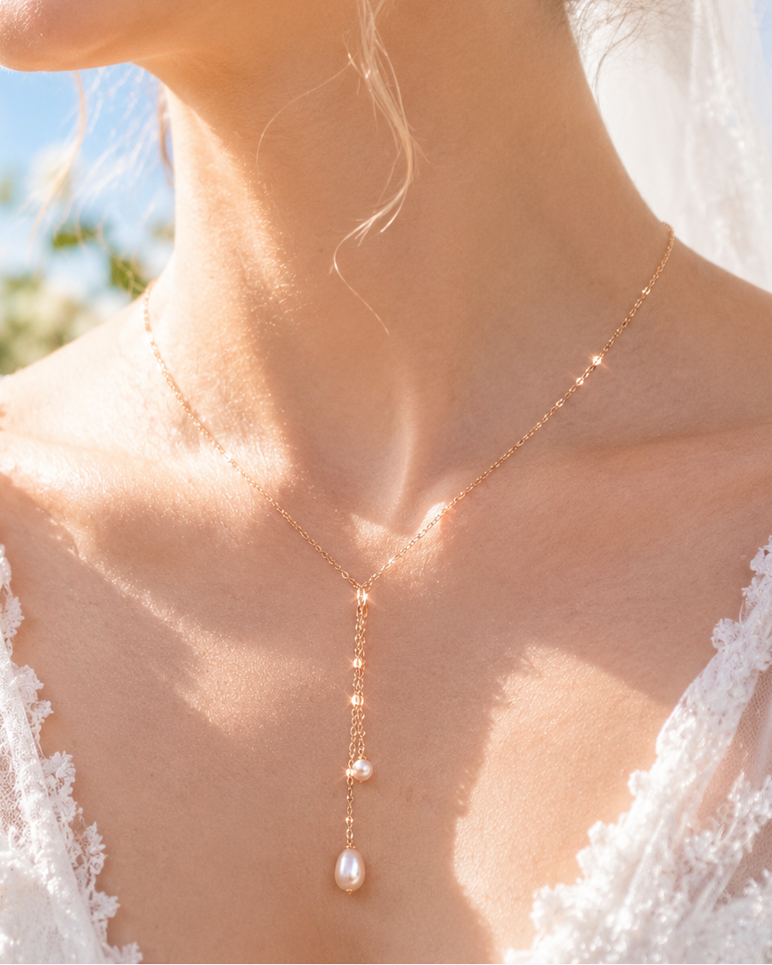 Close-up of a bride wearing a gold necklace with a pearl pendant, outdoors.
