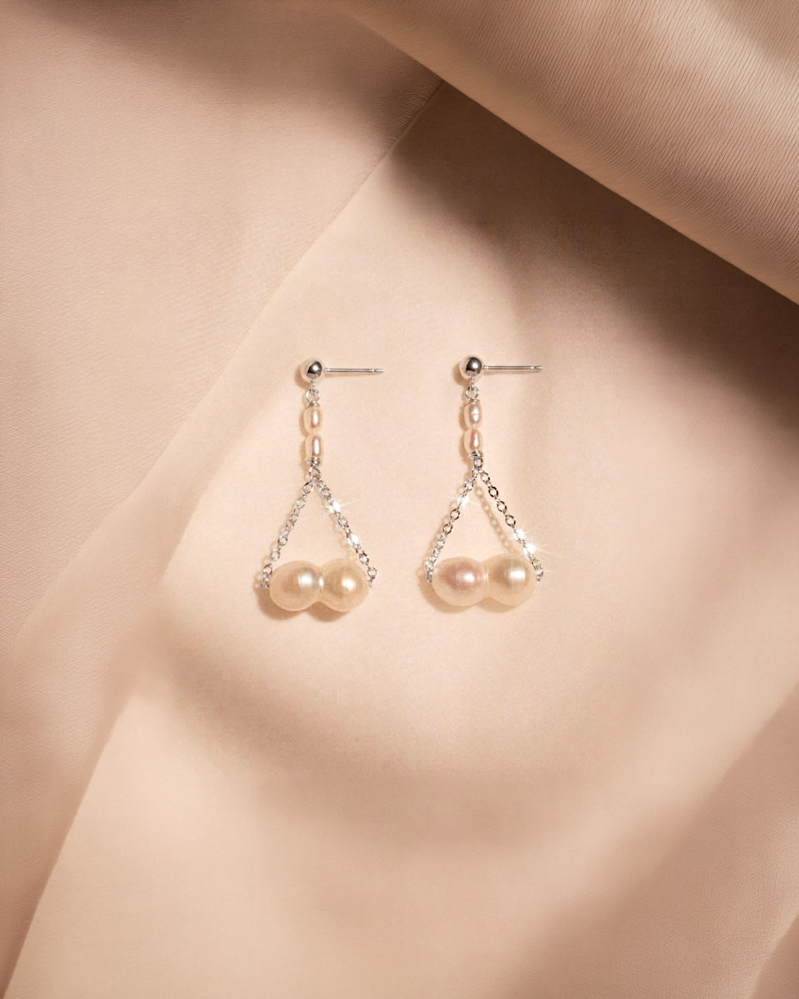 Pearl earrings on a soft beige fabric background