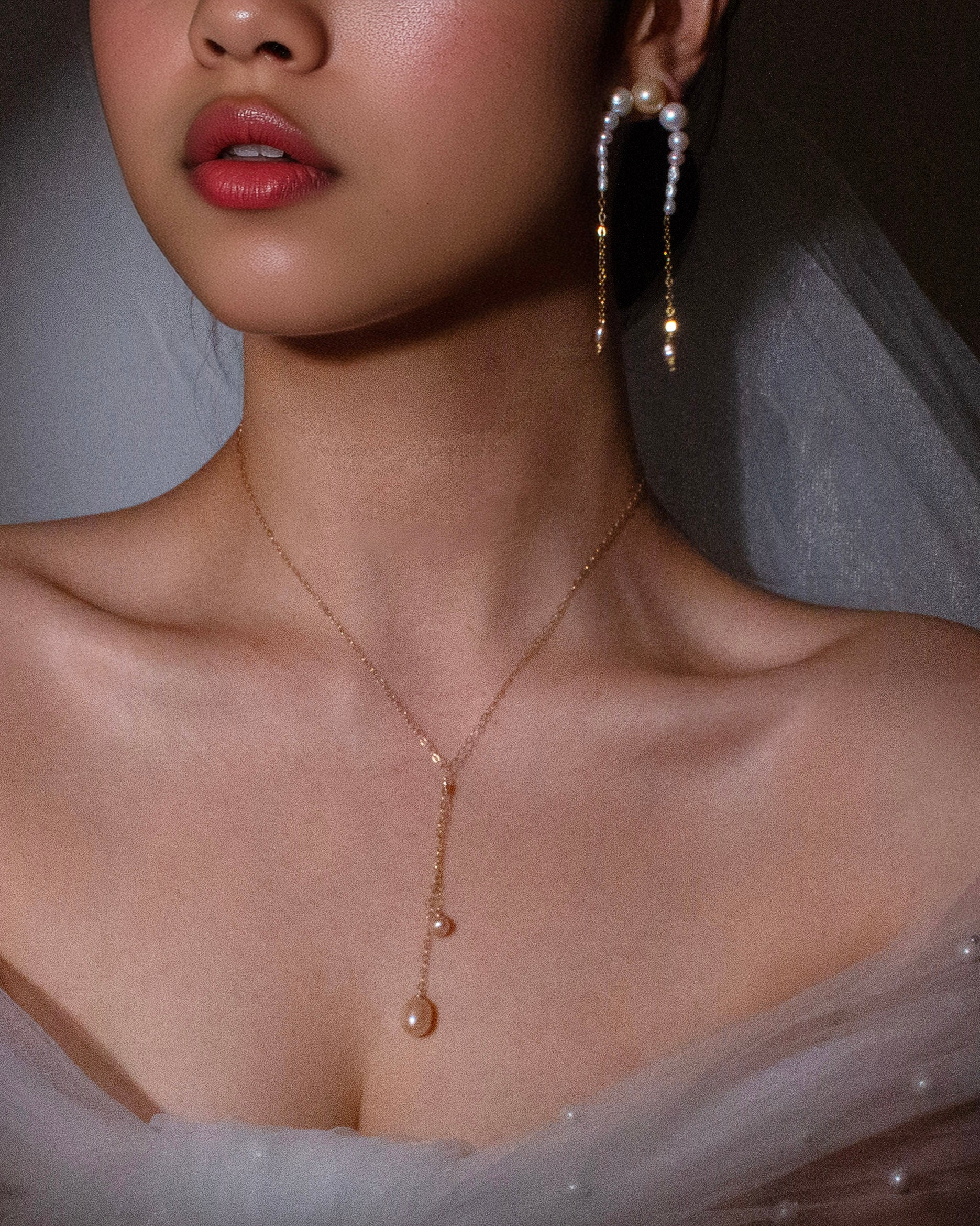 Close-up of a person wearing a delicate necklace and earrings with a soft focus background