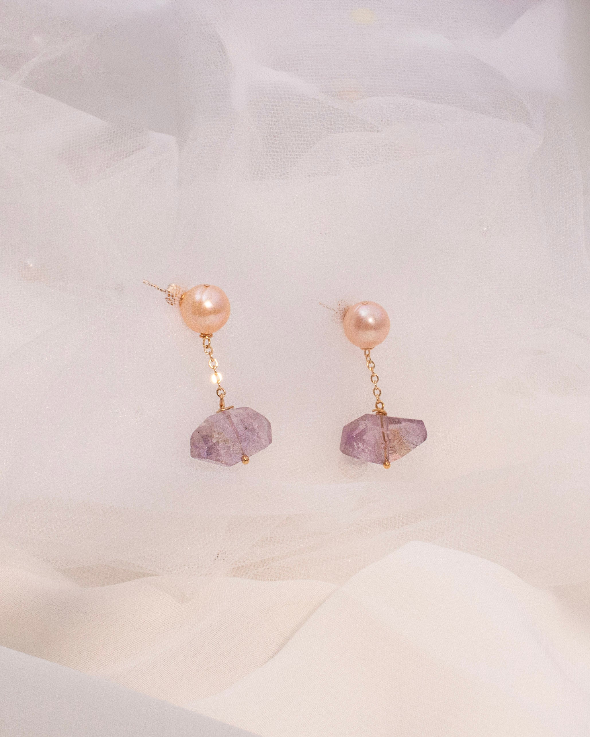 Pair of earrings with pink pearls and amethyst gemstones on a white background