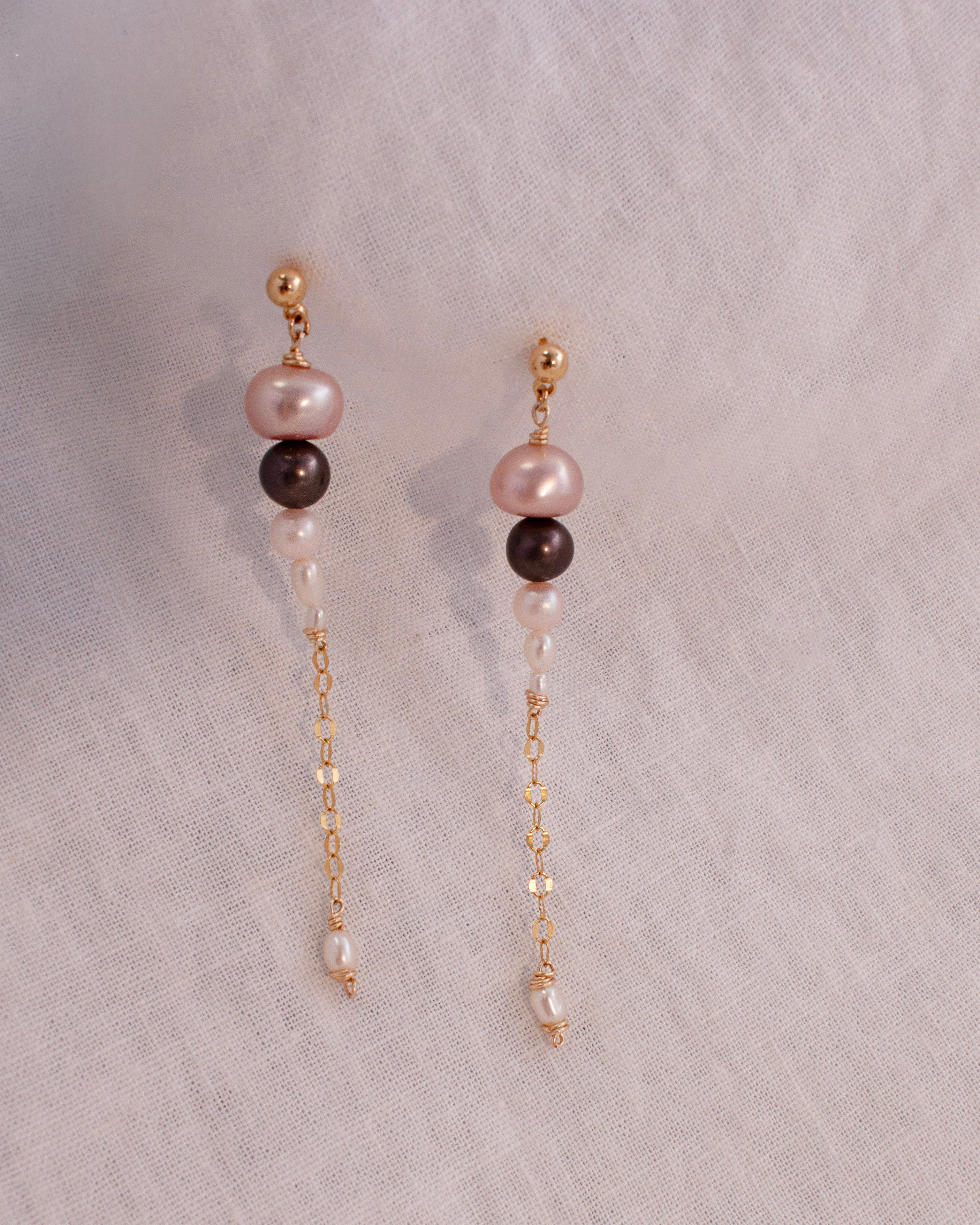 Pair of pearl earrings with gold chains on a light gray background