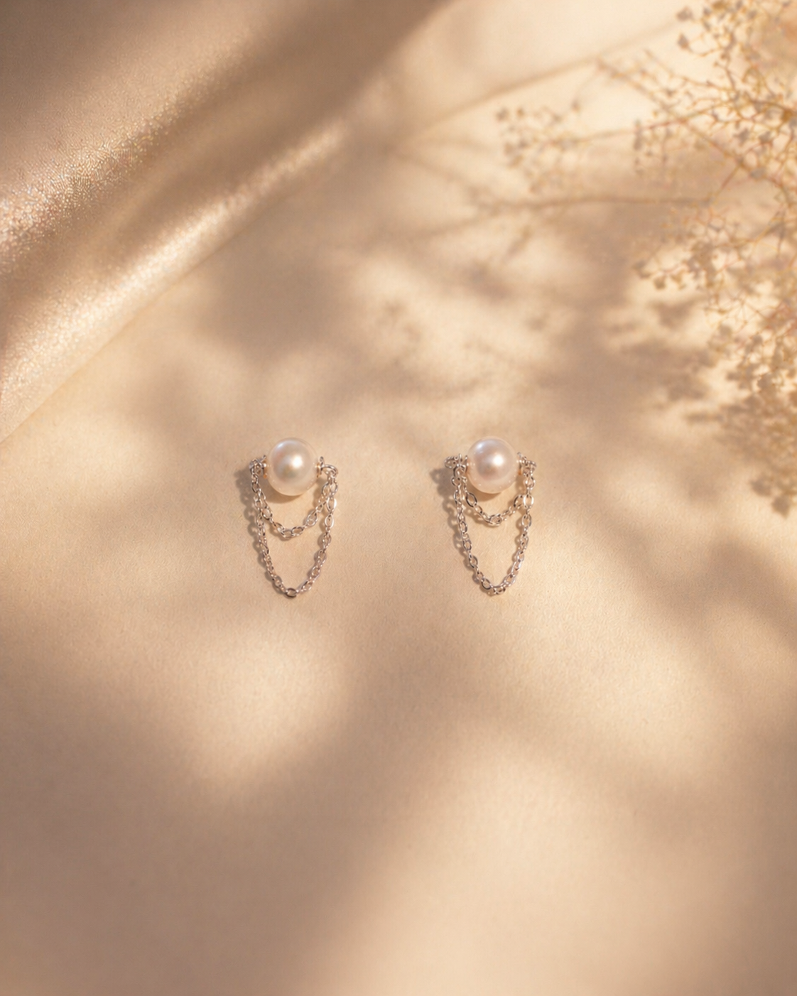 Pair of pearl earrings with chain details on a gold fabric background
