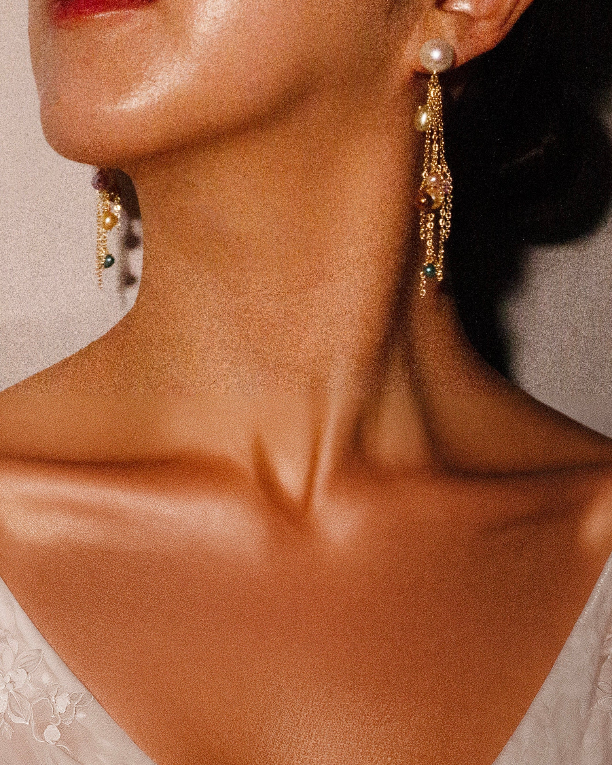 Close-up of a person wearing gold earrings with pearls and gemstones.