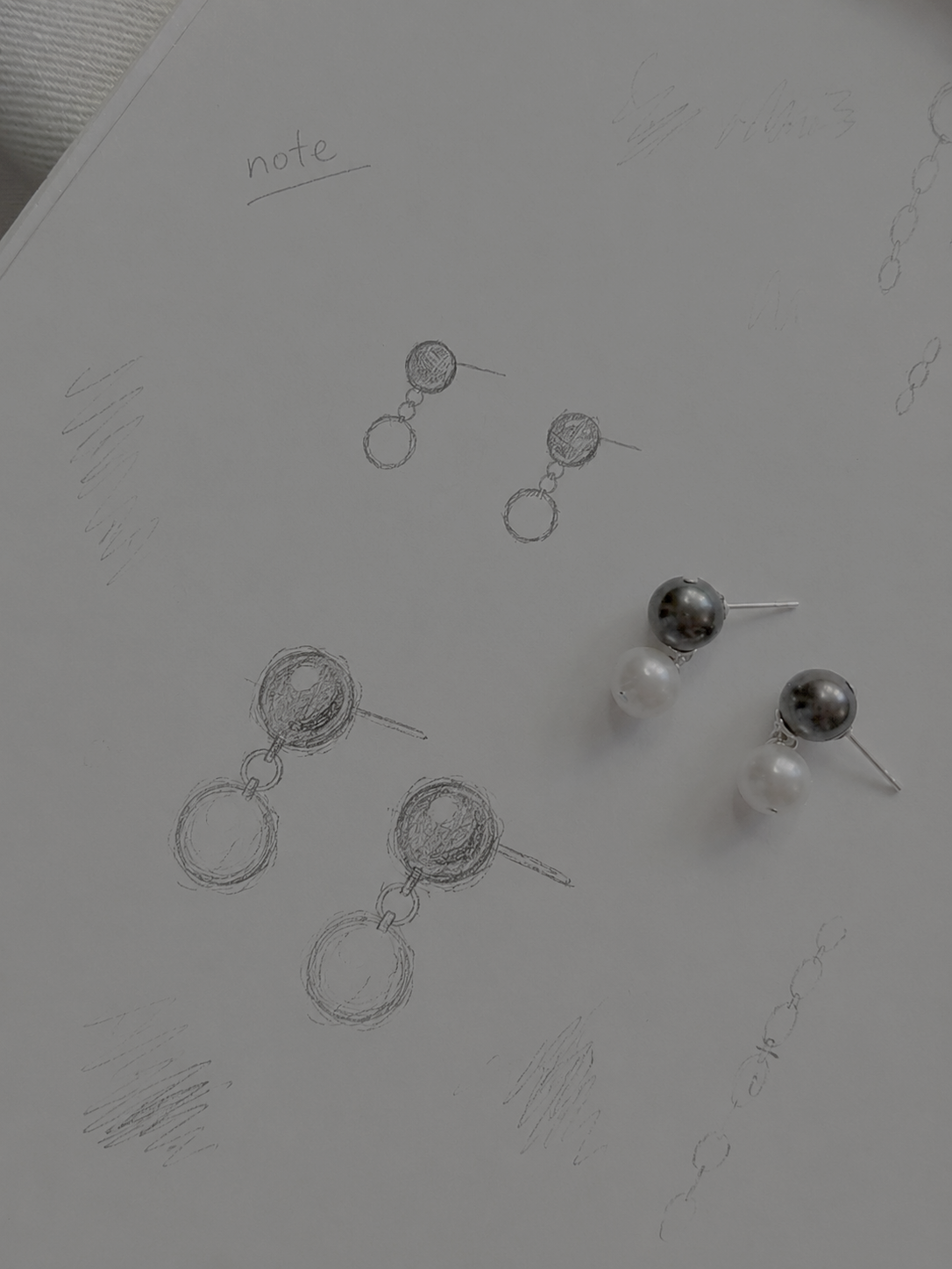Earrings on a surface with sketches of similar earrings nearby.